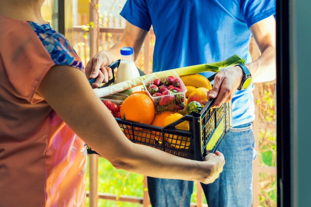 woman accepting groceries box from delivery man at home